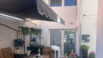 An outdoor patio with a table and chairs, a covered area, and potted plants.