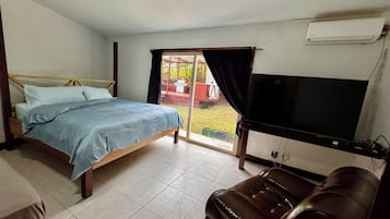 A bedroom with a bed, a television, a leather couch, and a sliding glass door leading to an outdoor area.