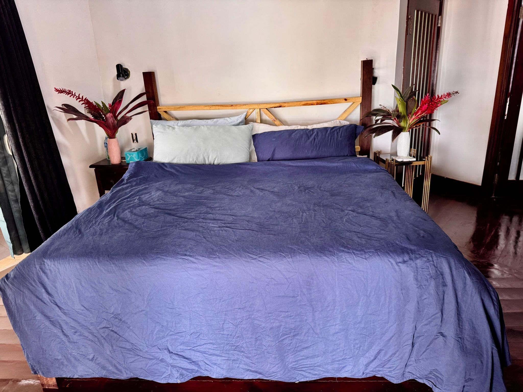 A bed with a wooden headboard, a blue bedspread, and two potted plants on either side.
