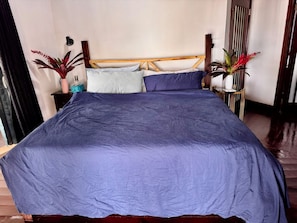A bed with a wooden headboard, a blue bedspread, and two potted plants on either side.