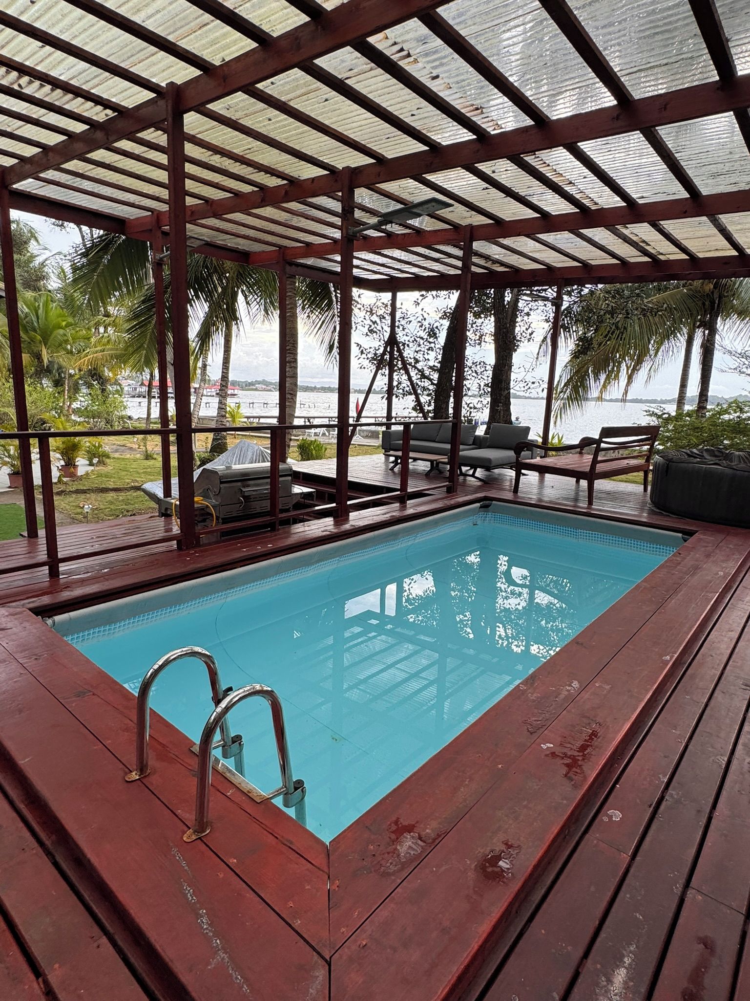 Piscina coberta com escada de metal, deck de madeira e mobiliário de exterior.