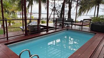 Piscina coberta com escada de metal, deck de madeira e mobiliário de exterior.