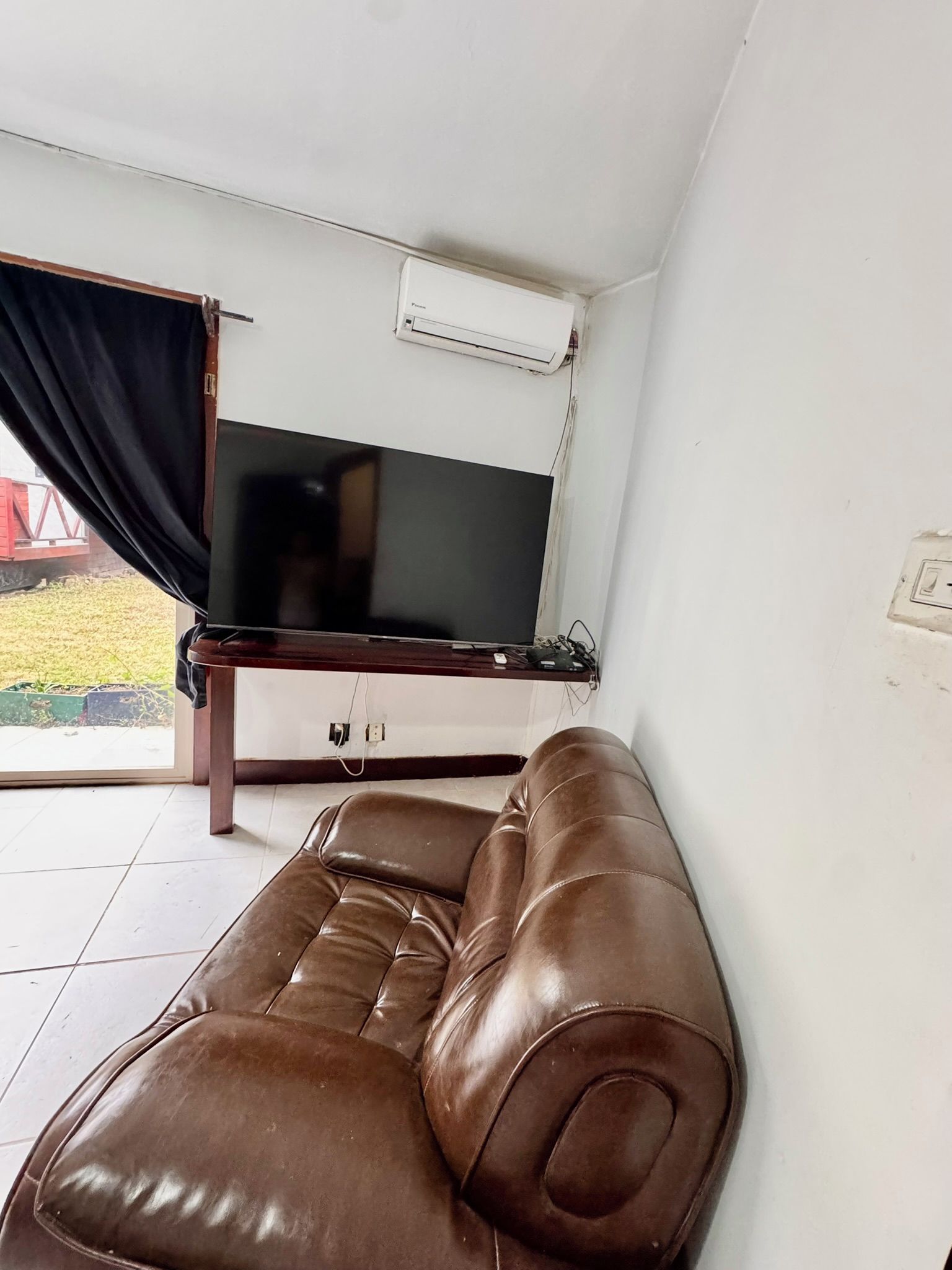 Een woonkamer met een bruine leren bank, een flatscreentelevisie aan de muur en een airconditioningsysteem.
