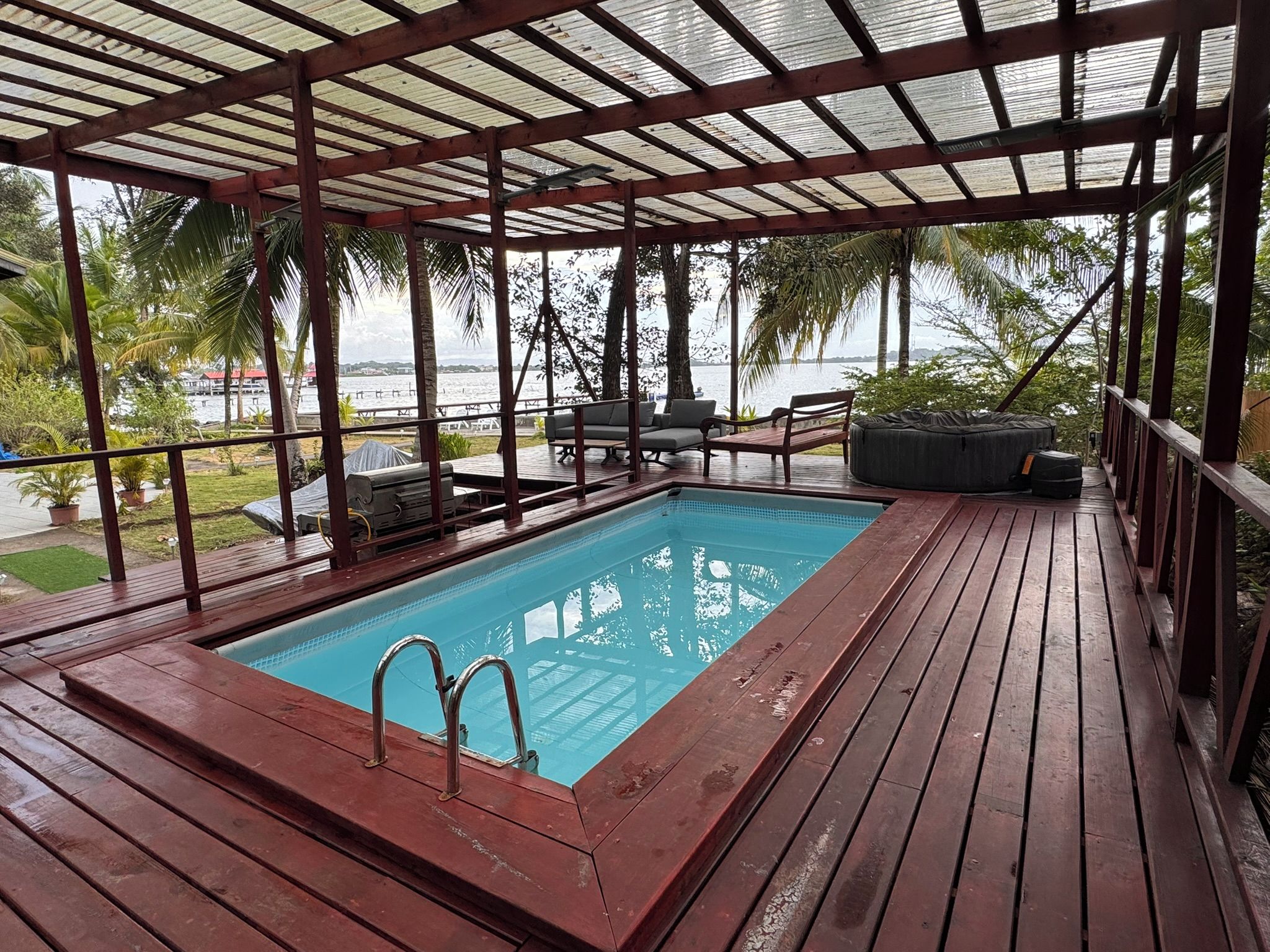 Piscina coberta ao ar livre com deck de madeira, área de estar com assentos e vista para o mar.