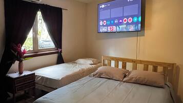 Quarto de hotel com duas camas, ventoinha no teto, ar condicionado, televisão presa à parede e janela com cortinas.