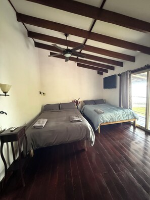 Una habitación con dos camas, ventilador de techo, lámpara y ventana con cortinas.