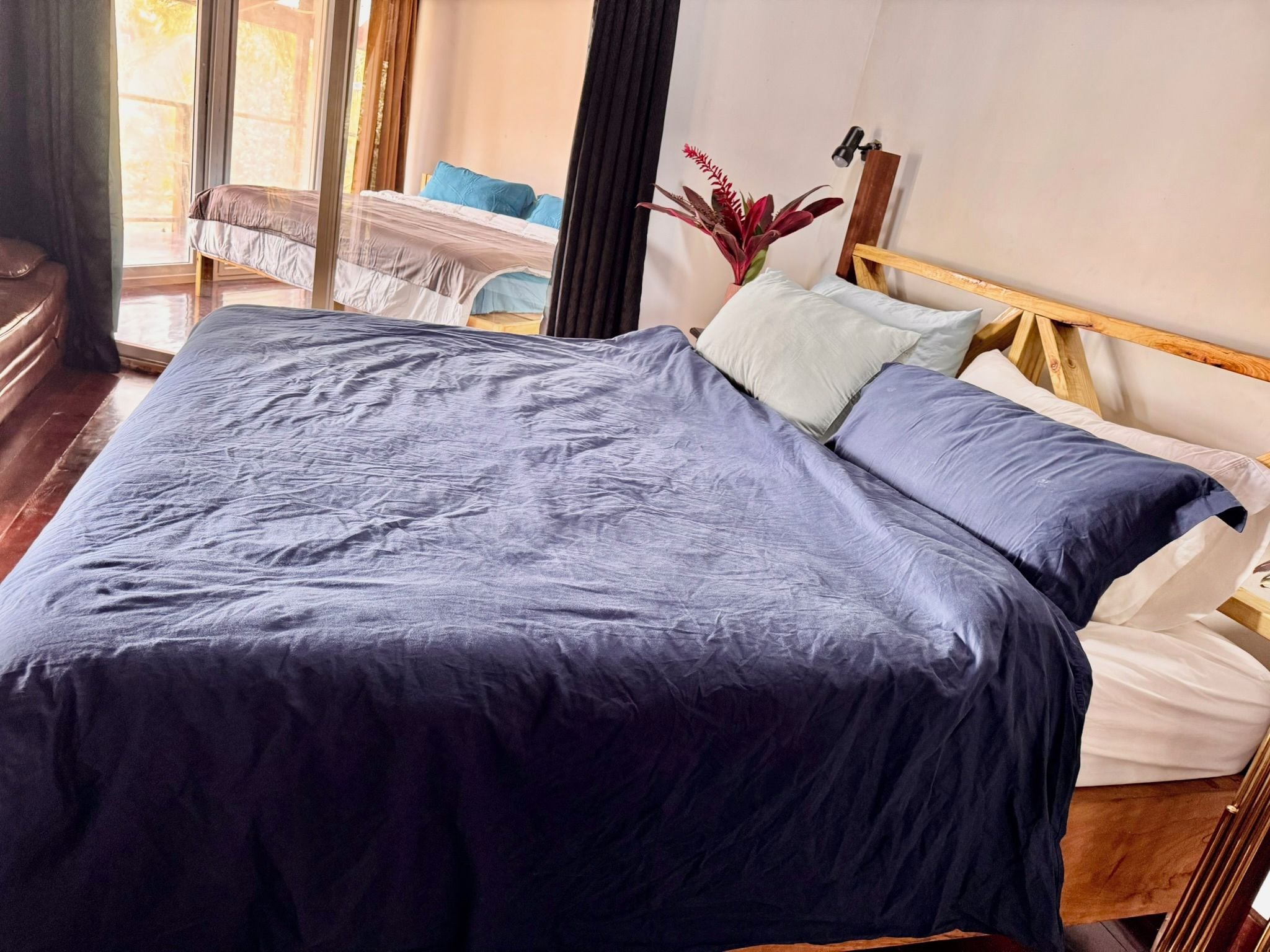 A bed with a dark blue bedspread and pillows, a wooden headboard, and a potted plant on the nightstand.