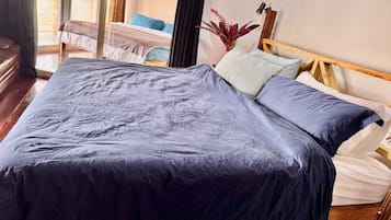 A bed with a dark blue bedspread and pillows, a wooden headboard, and a potted plant on the nightstand.
