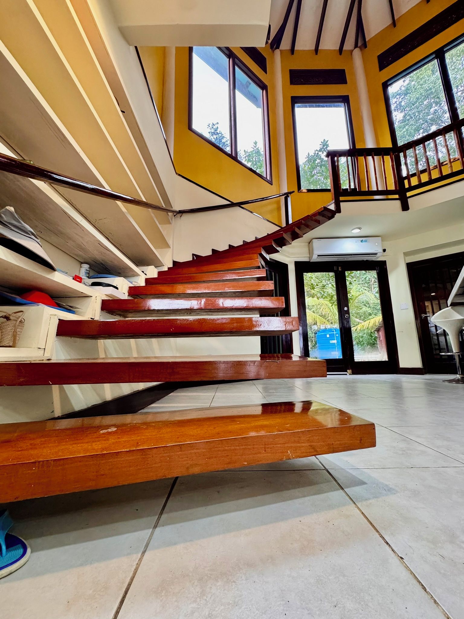 A spacious interior with a central staircase, large windows, and a view of greenery outside.