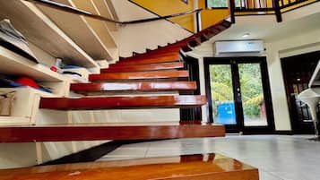 A spacious interior with a central staircase, large windows, and a view of greenery outside.