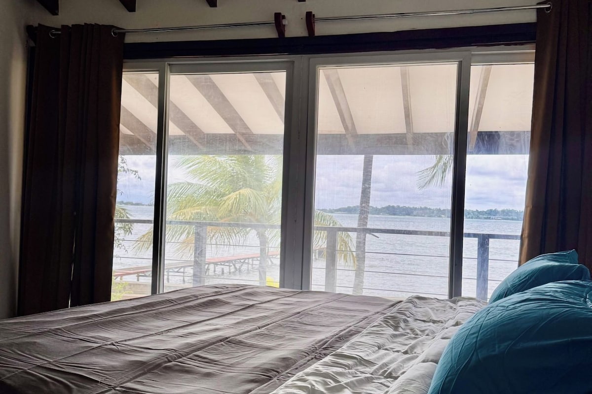 A bed with a view of the sea through large windows.