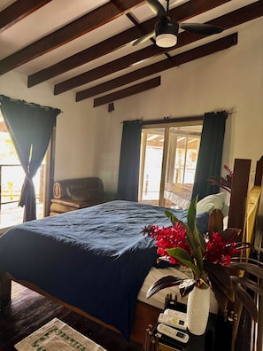 A room with a bed, a desk with a vase of flowers, and a ceiling fan. - Casa Maria Beach & Boat Club (Bocas del Toro)