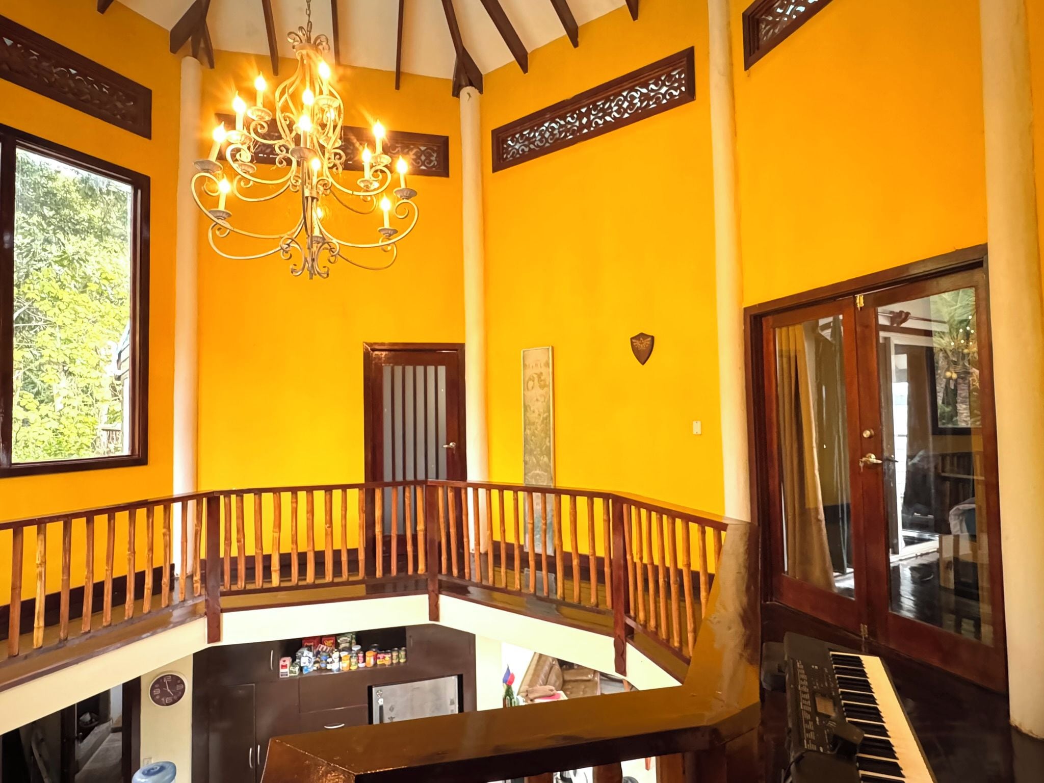 Una habitación con pared amarilla, una araña, un piano y un balcón con barandilla de madera.