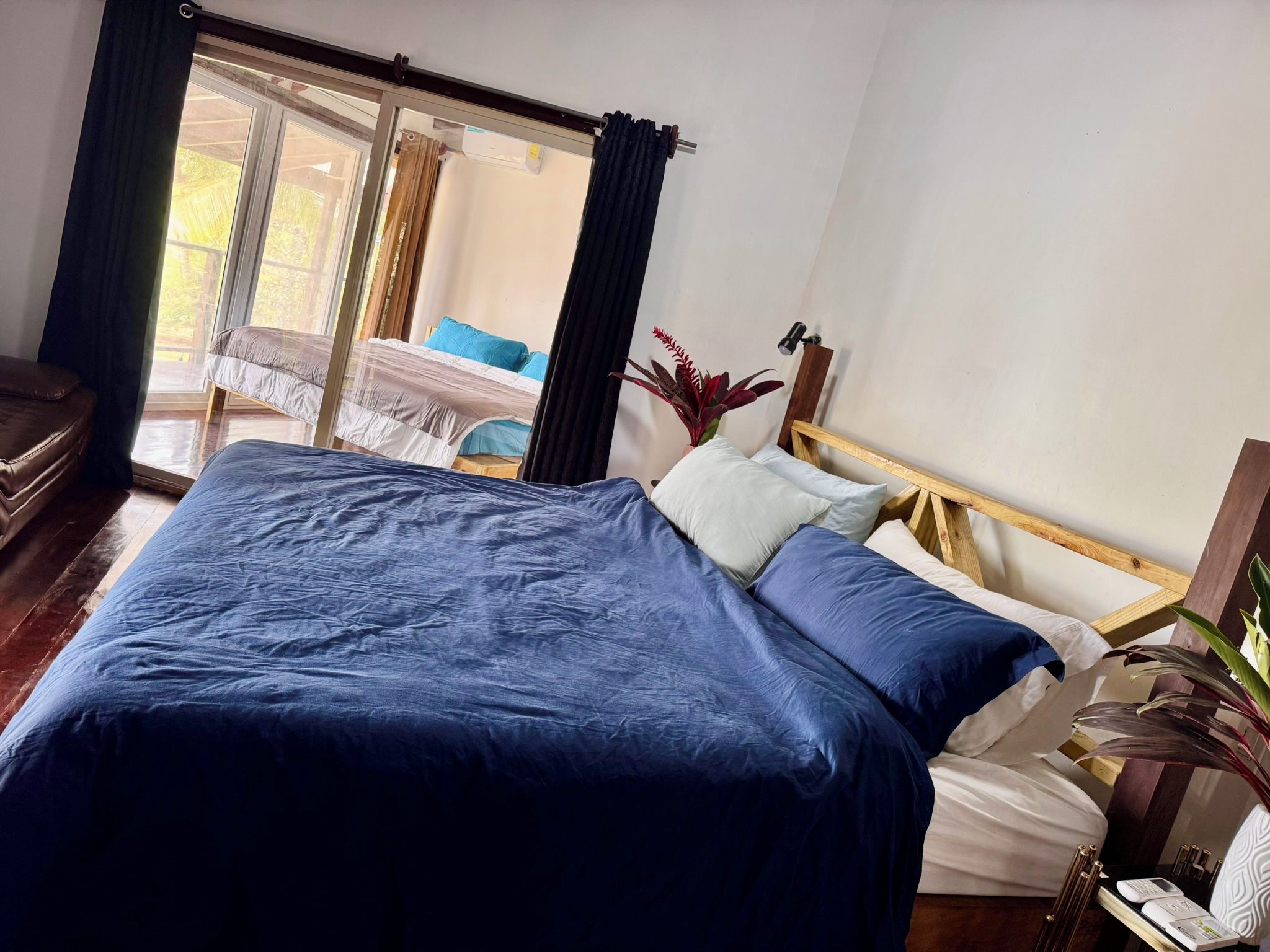 Une chambre à coucher avec un grand lit, une tête de lit en bois, une petite table avec une lampe et une fenêtre avec des rideaux.