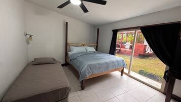 Un dormitorio con cama, una cama adicional, ventilador de techo y vista al exterior.