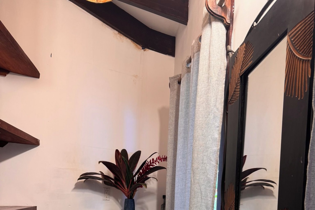 Un baño con inodoro, lavabo y espejo. Hay una repisa con una planta y una botella.