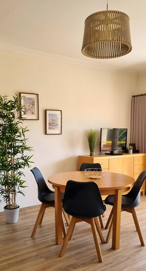 Een eetgedeelte met een houten tafel en stoelen, een hanglamp, een televisie en ingelijste foto's aan de muur.