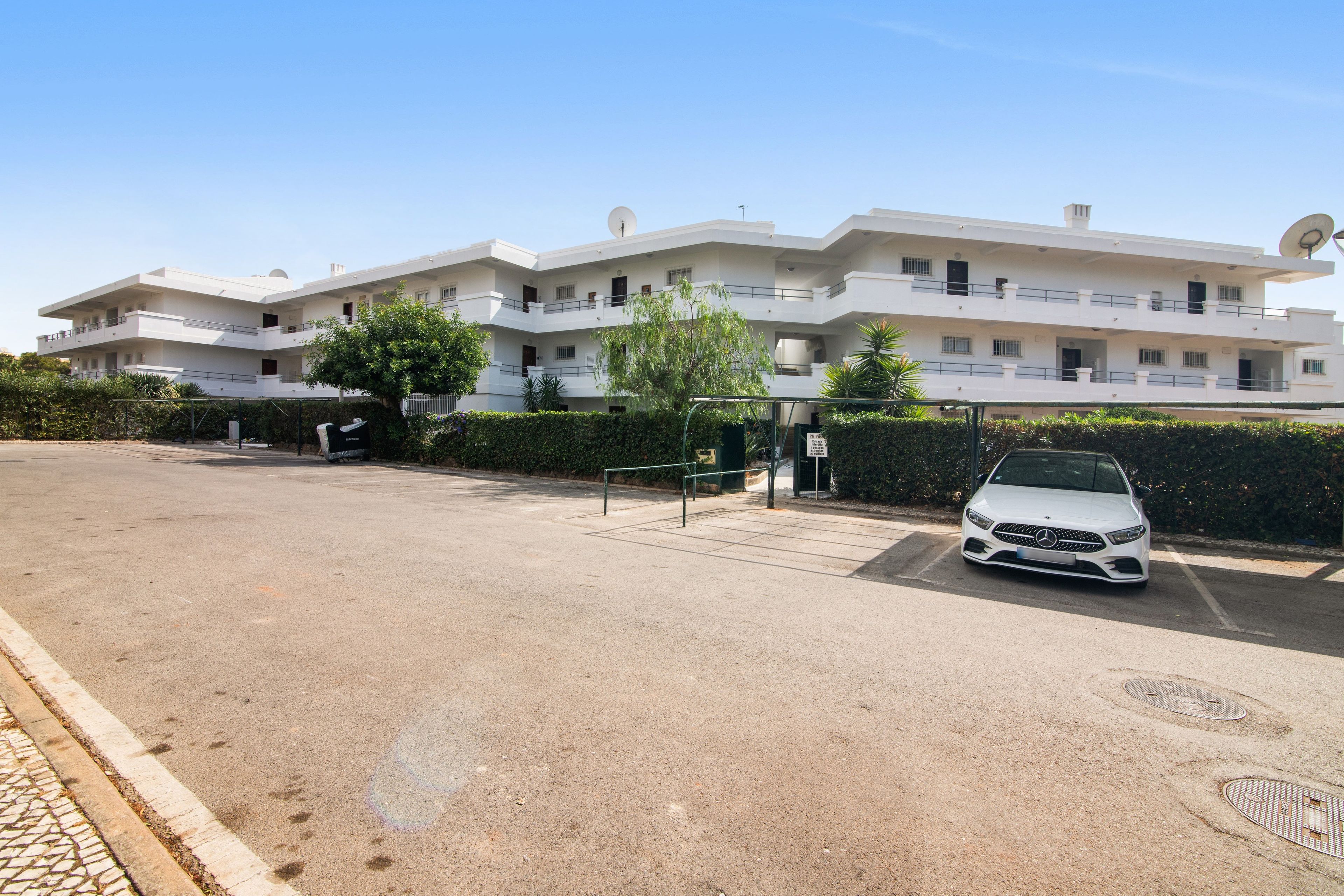 Um edifício de vários andares com fachada plana, entrada gradeada e um carro estacionado.