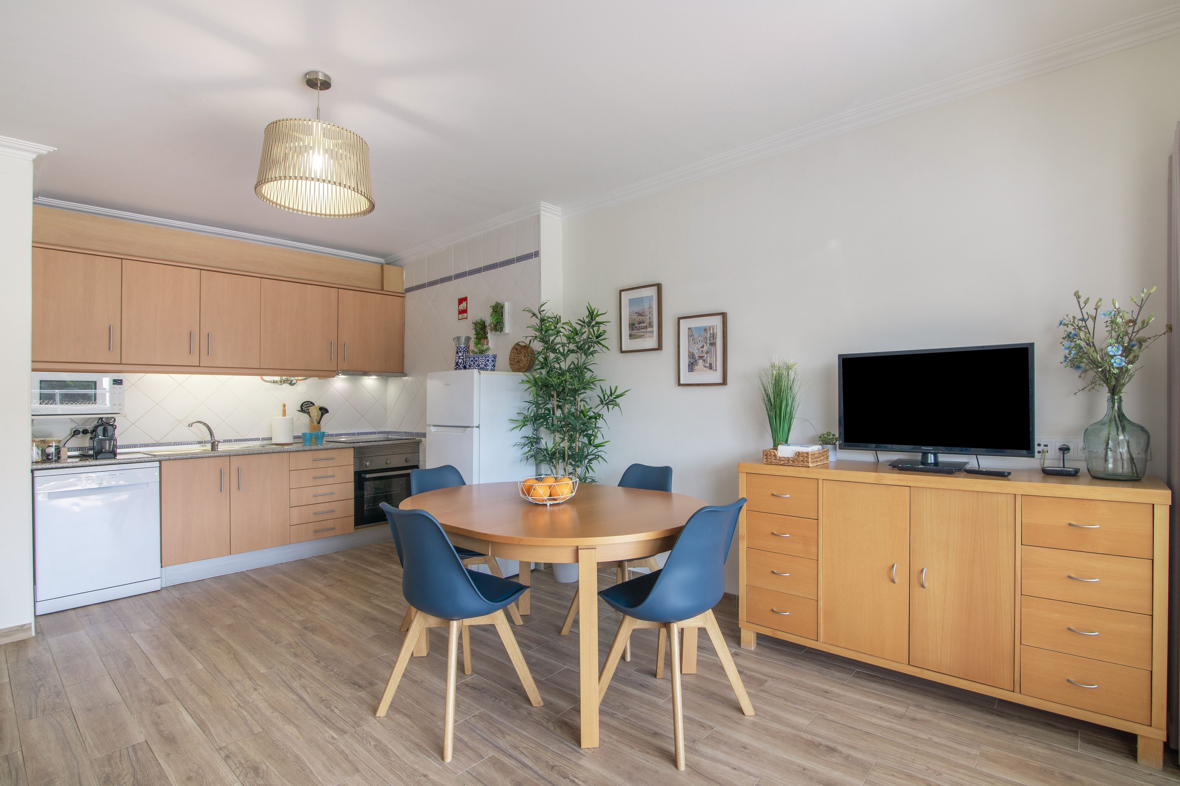 Una cucina moderna con mobili in legno, un tavolo da pranzo con sedie, una televisione e una pianta.