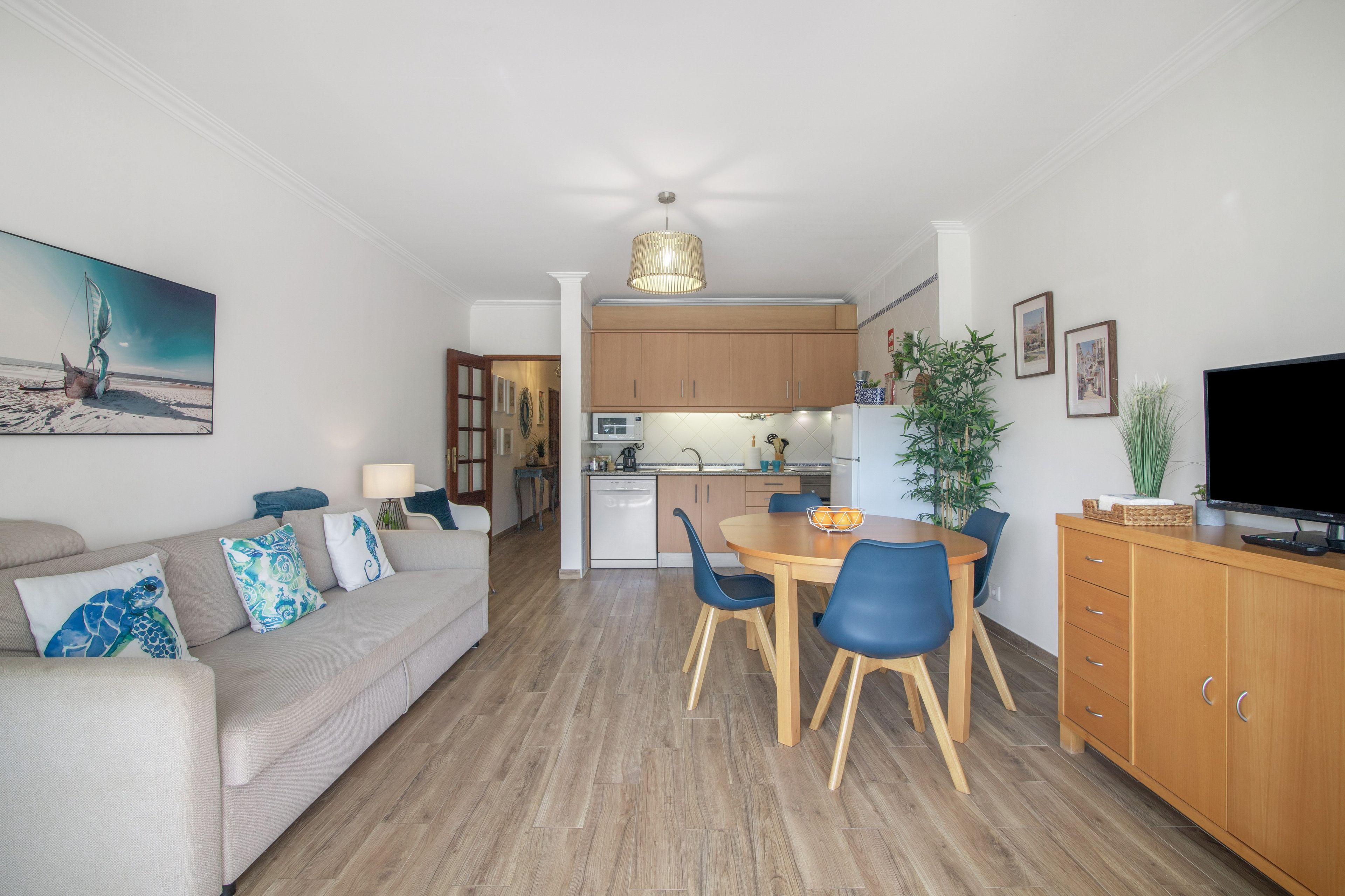 Een moderne woonkamer met een bank, een eettafel met stoelen, een keuken met kasten en een televisie.