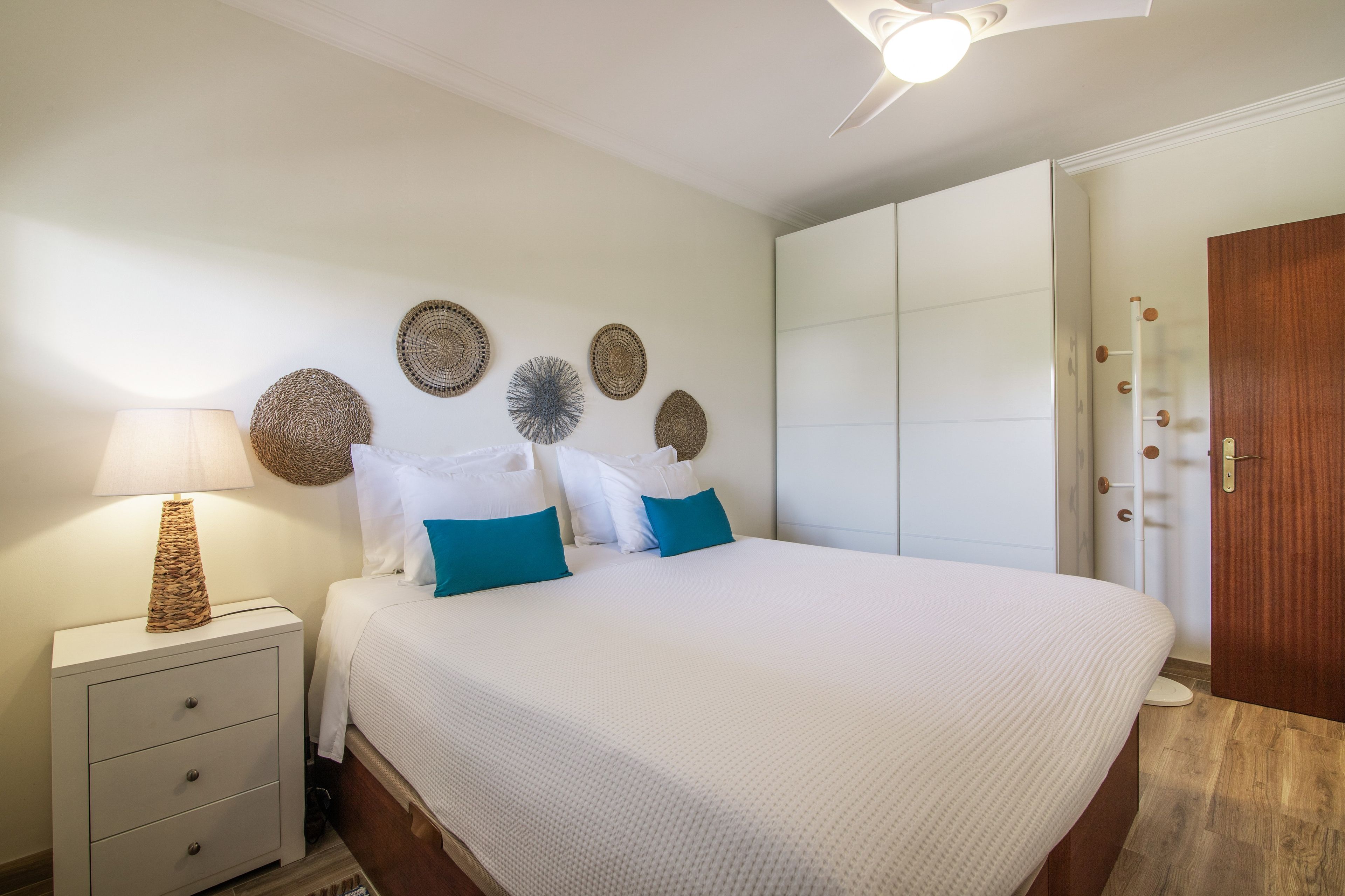 Een slaapkamer met een bed, nachtkastjes, een lamp, decoratieve wanddecoraties en een kledingkast.