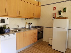 Een keuken met houten kastjes, een magnetron, een fornuis, een spoelbak en een koelkast.