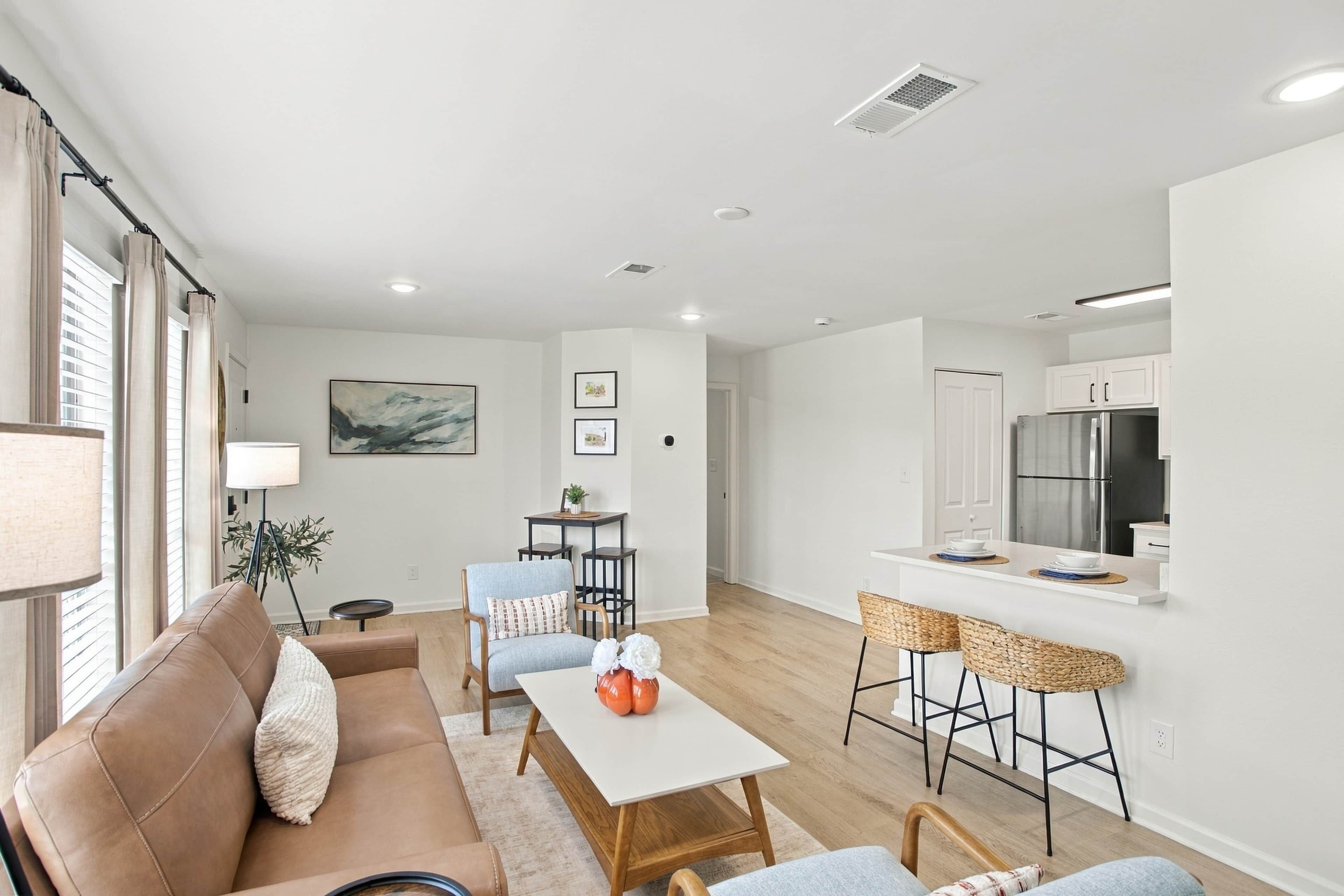 Una sala moderna con sofá, una mesa de comedor y una cocina con refrigerador y taburetes de bar.