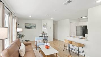 Una sala moderna con sofá, una mesa de comedor y una cocina con refrigerador y taburetes de bar.
