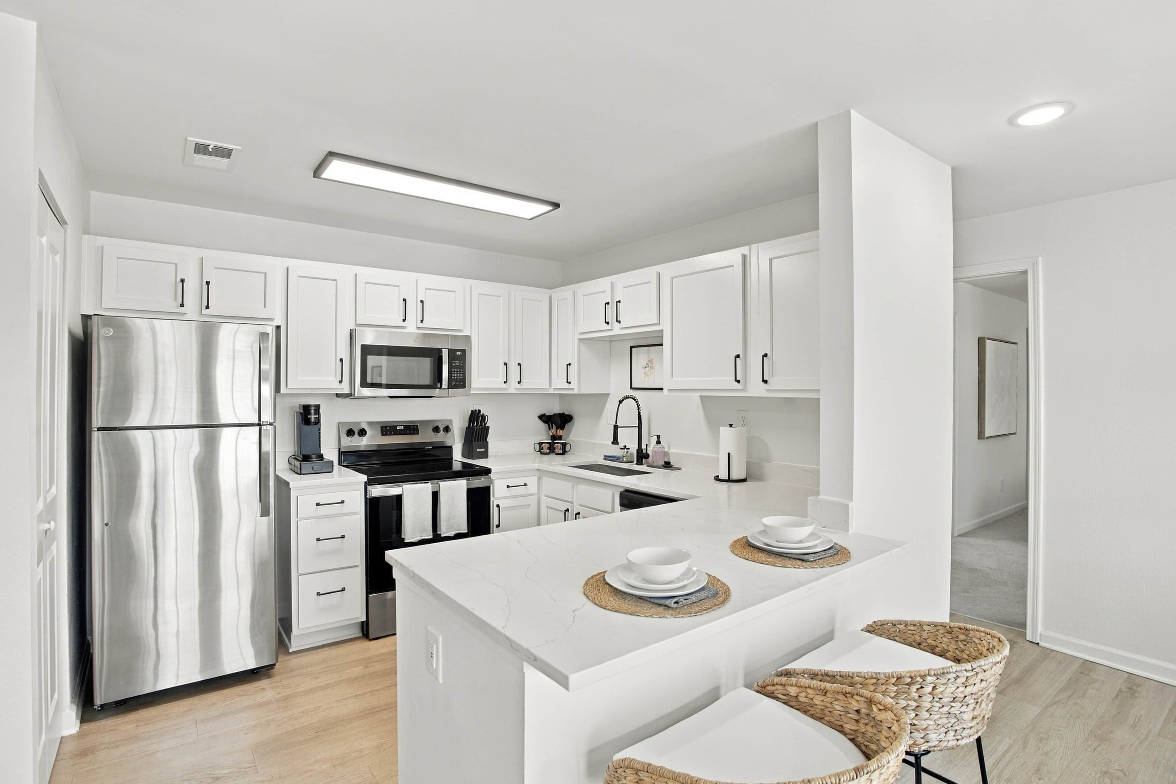 A modern kitchen with white cabinetry, stainless steel appliances, and a central island with seating.