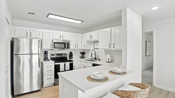 A modern kitchen with white cabinetry, stainless steel appliances, and a central island with seating.