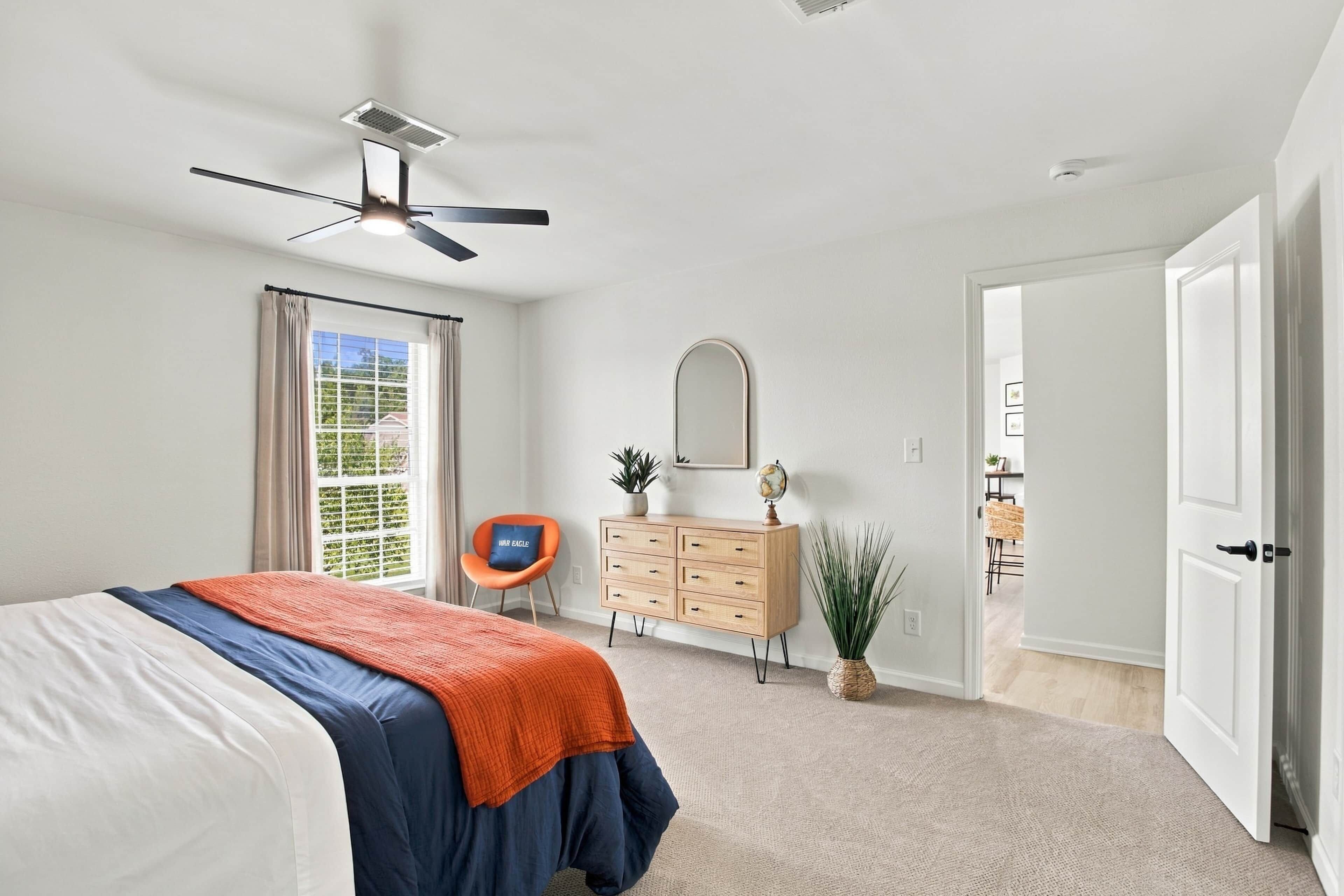 Un dormitorio con cama, ventilador de techo, cómoda, silla, un globo terráqueo y una puerta que da a otra habitación.