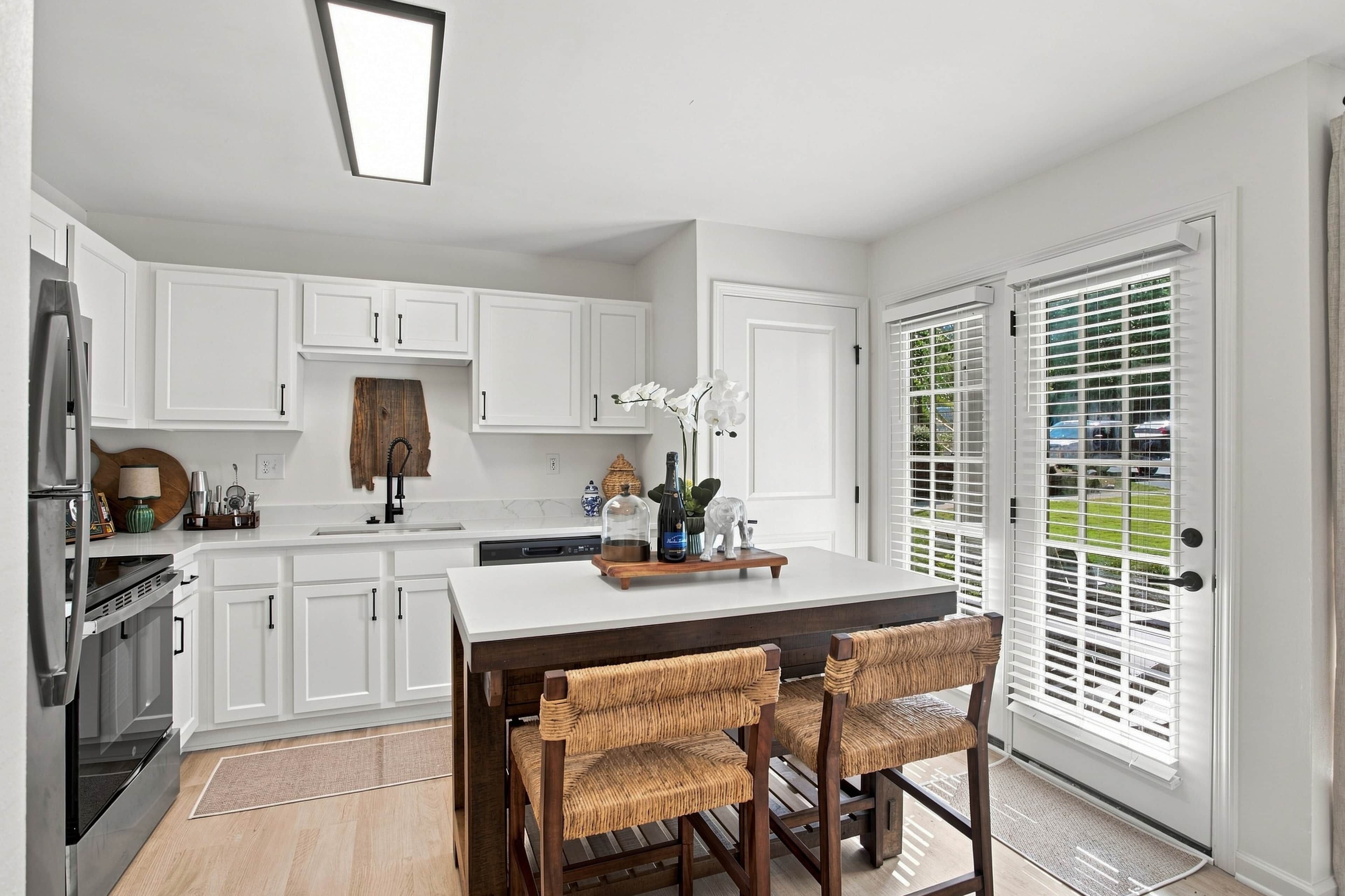 A modern kitchen with white cabinetry, a central island, and a dining area with wicker chairs.