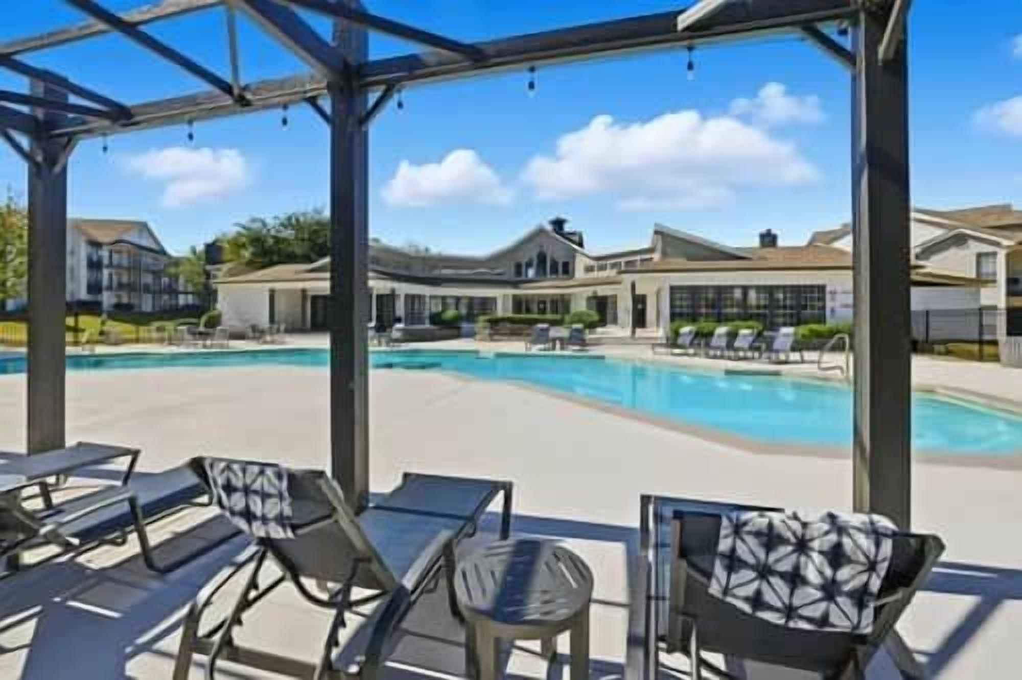 Un área de piscina con sillones de descanso y una zona de estar cubierta.