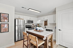Una cocina moderna con armarios blancos, electrodomésticos de acero inoxidable y una mesa de comedor de madera con sillas.