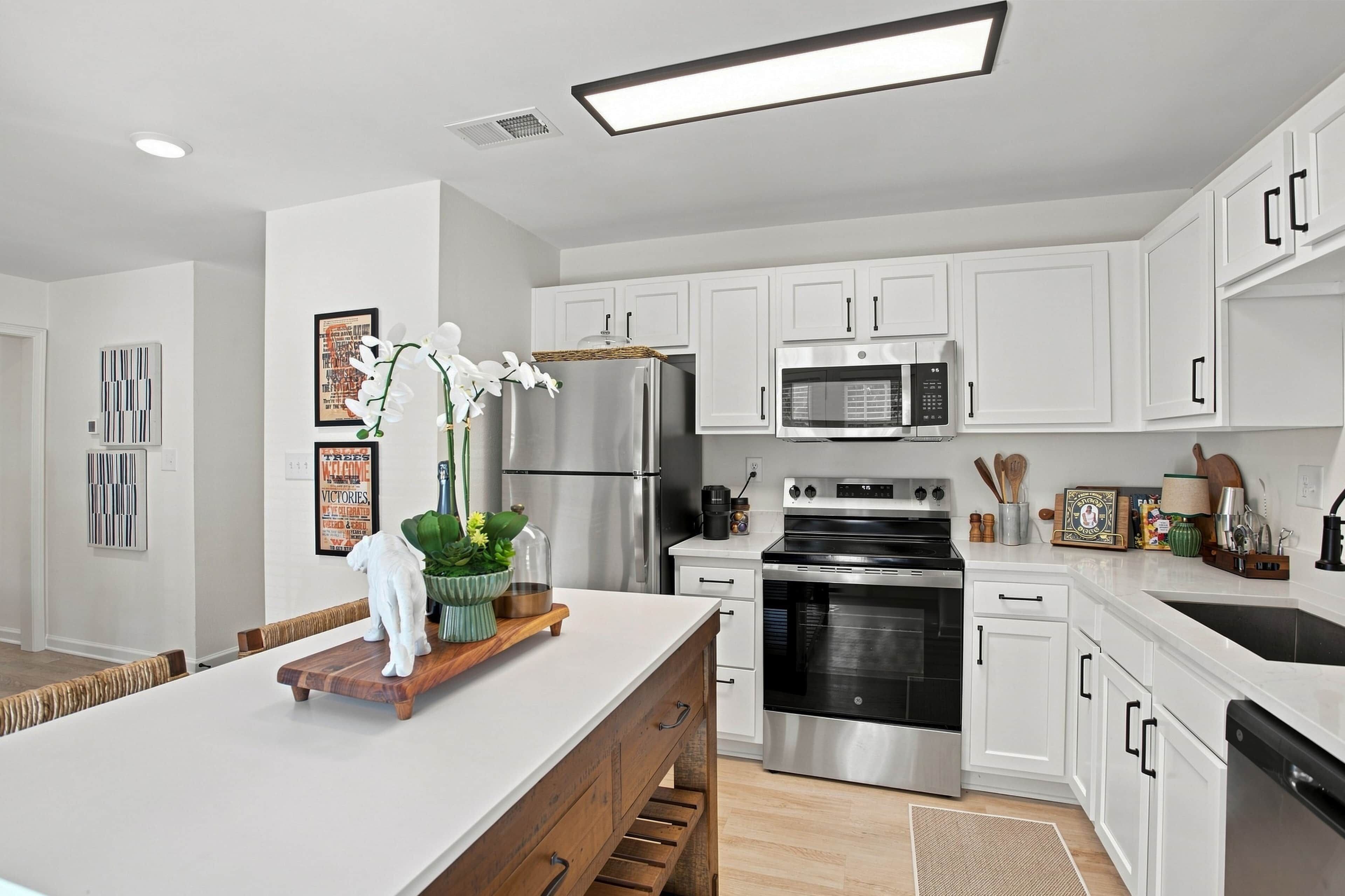 A modern kitchen with white cabinetry, stainless steel appliances, and a central island with a plant and decorative items.