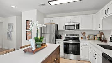 A modern kitchen with white cabinetry, stainless steel appliances, and a central island with a plant and decorative items.