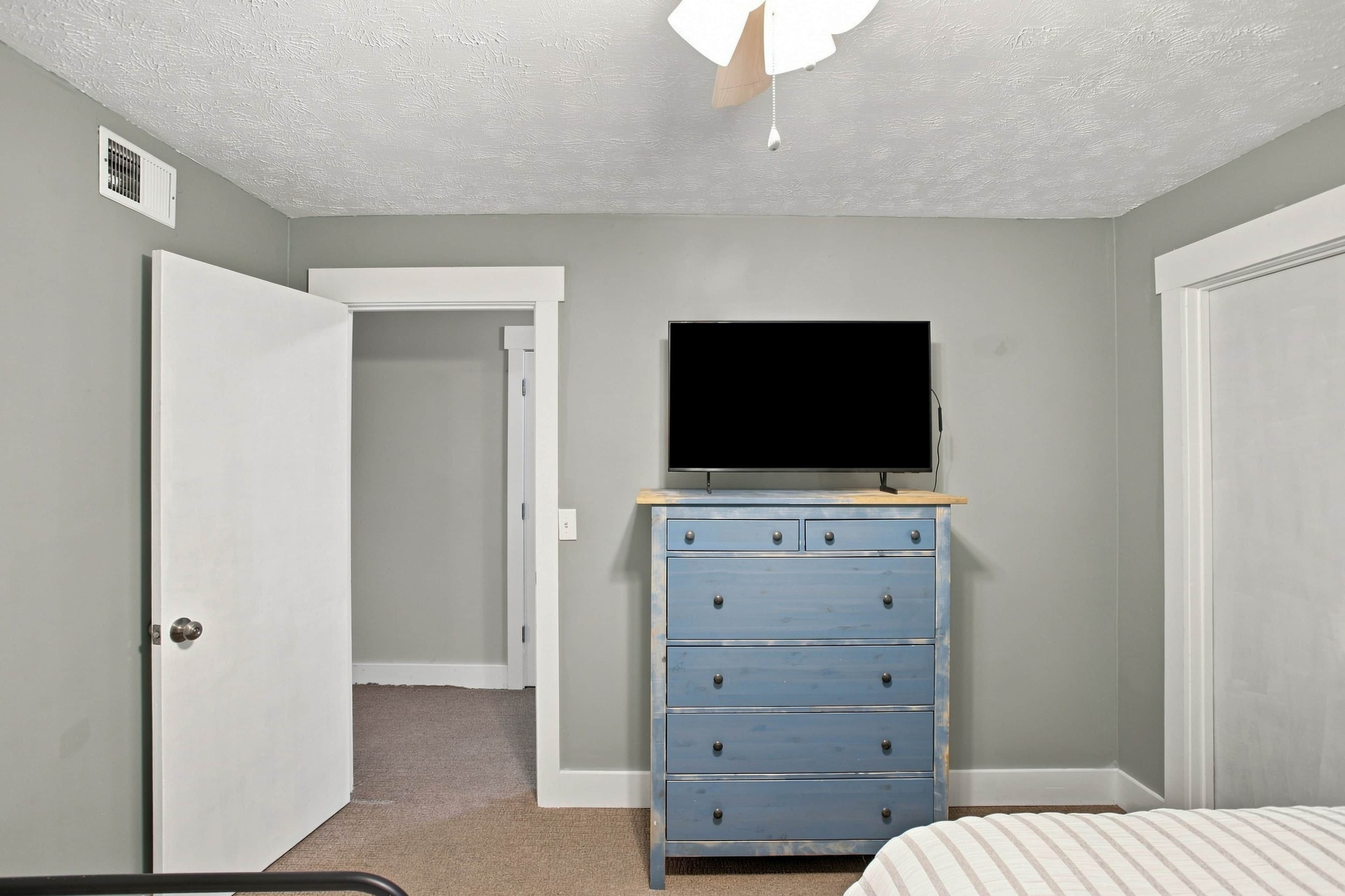 Un dormitorio con cama, cómoda, televisor encima y una puerta que da a otra habitación.