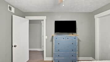 Un dormitorio con cama, cómoda, televisor encima y una puerta que da a otra habitación.