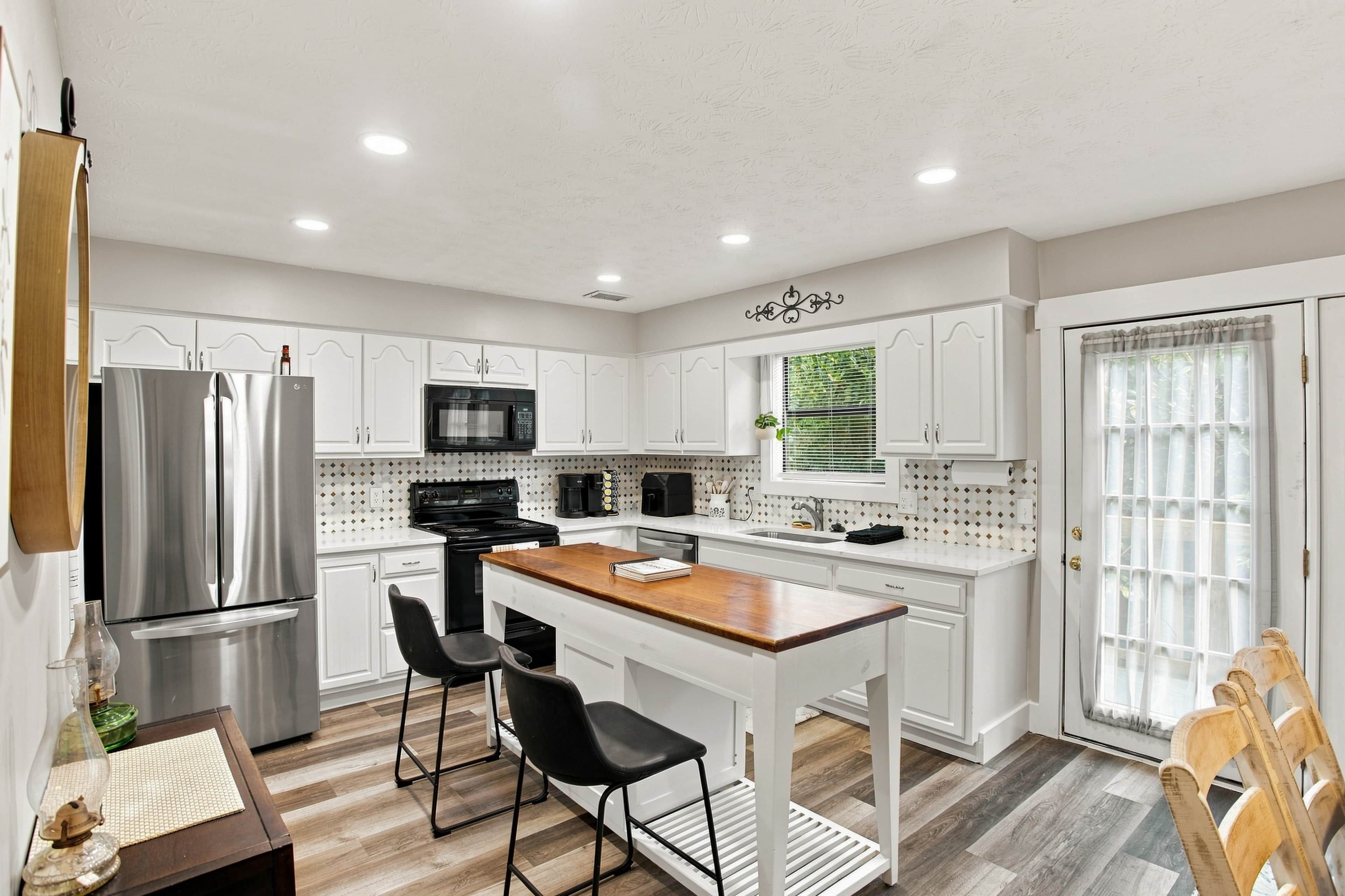 A modern kitchen with white cabinets, stainless steel appliances, a wooden island, and a dining area with chairs.