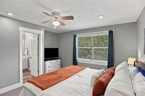 A bedroom with a bed, a television, a window with blinds, a ceiling fan, and a door leading to another room. - Tiger Den for 10-Blocks to Campus (Auburn)