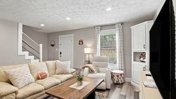 A living room with a sofa, a coffee table, a TV, and a staircase.