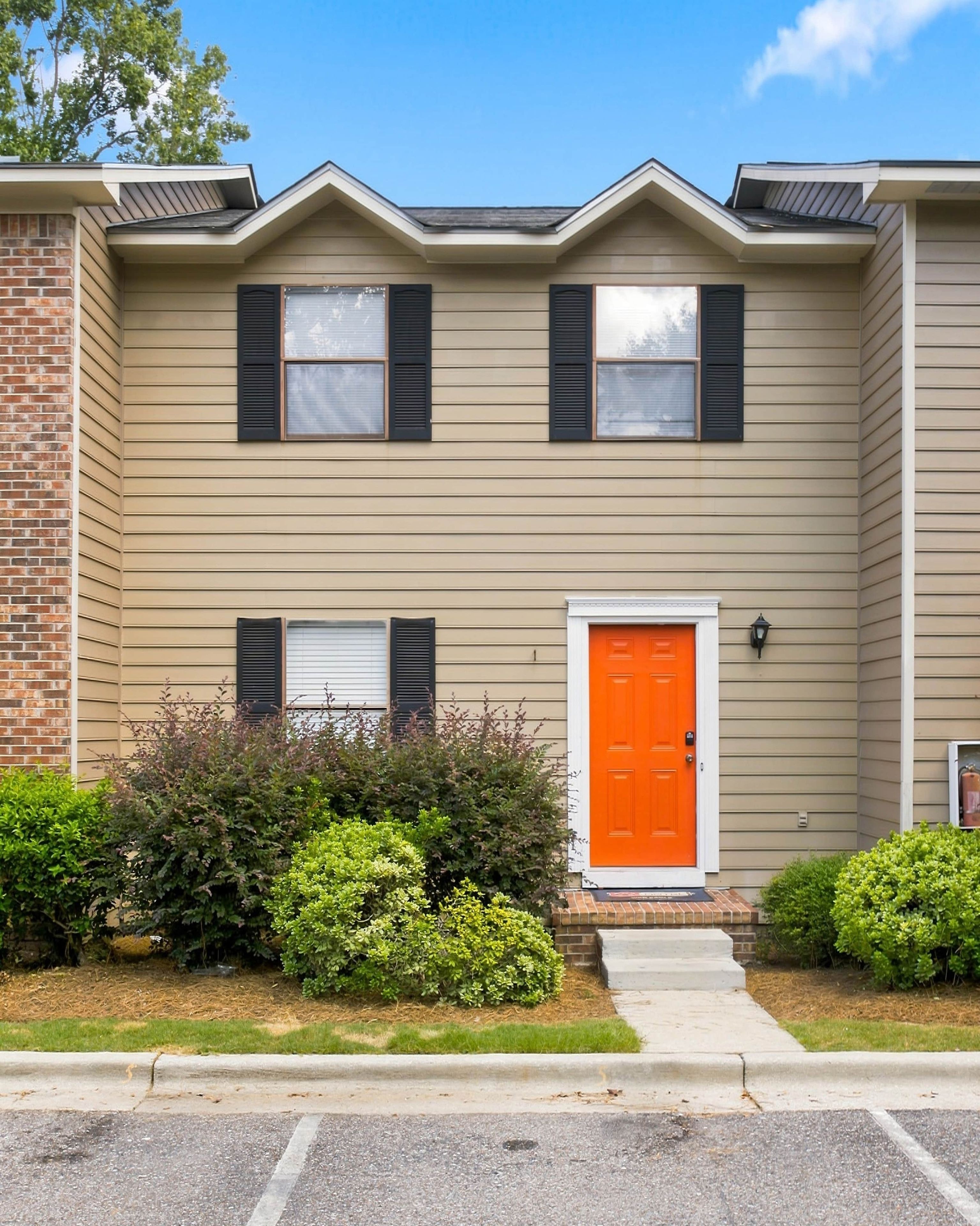 A two-story building with a brick facade, a beige exterior, and a bright orange door.