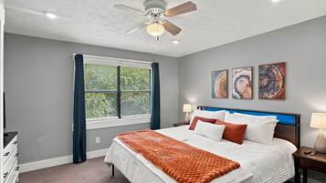 A bedroom with a bed, a ceiling fan, a window with curtains, and wall art.