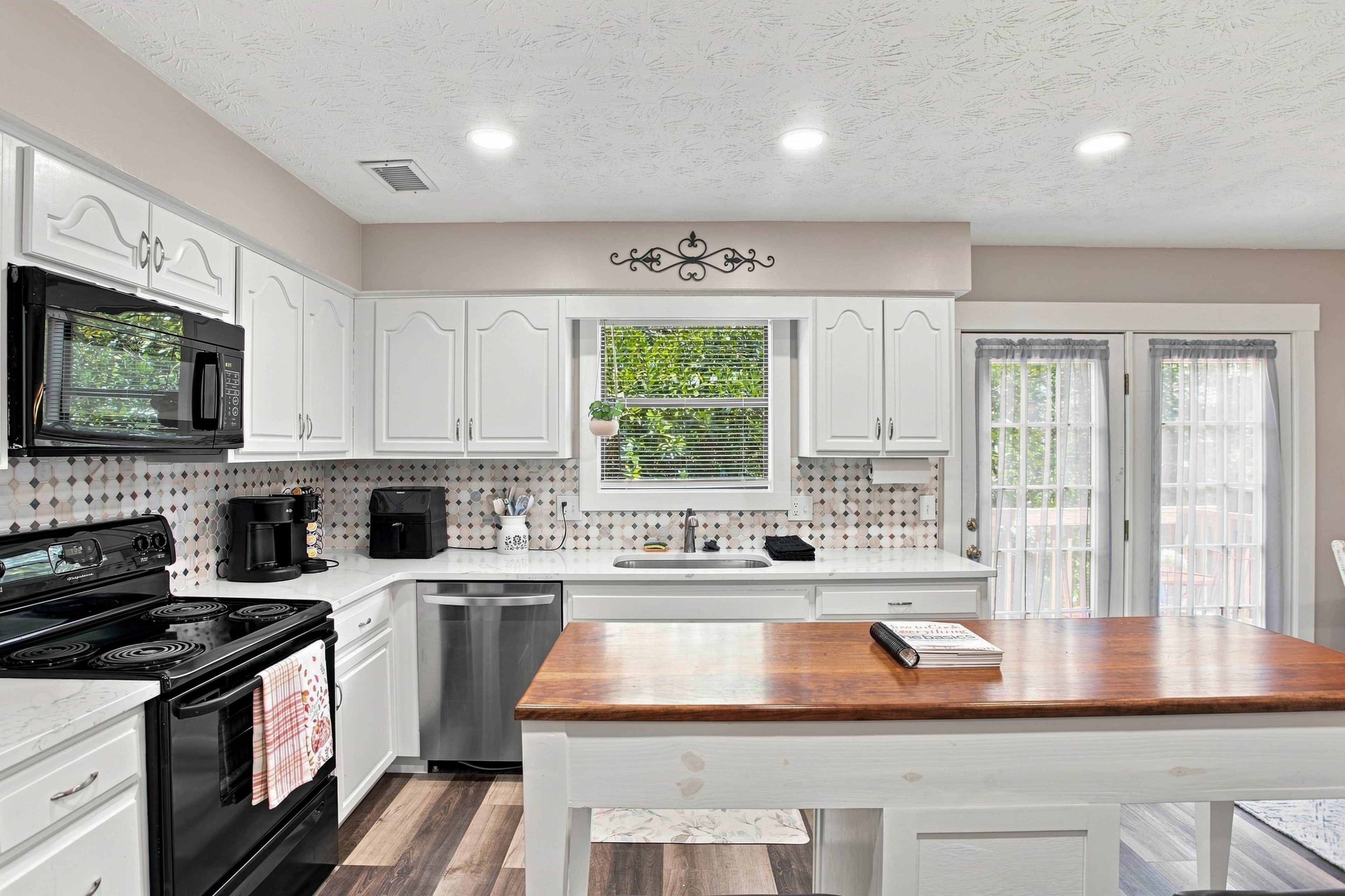 A modern kitchen with white cabinetry, a wooden countertop, a built-in oven, a coffee maker, and a window with a view of greenery.