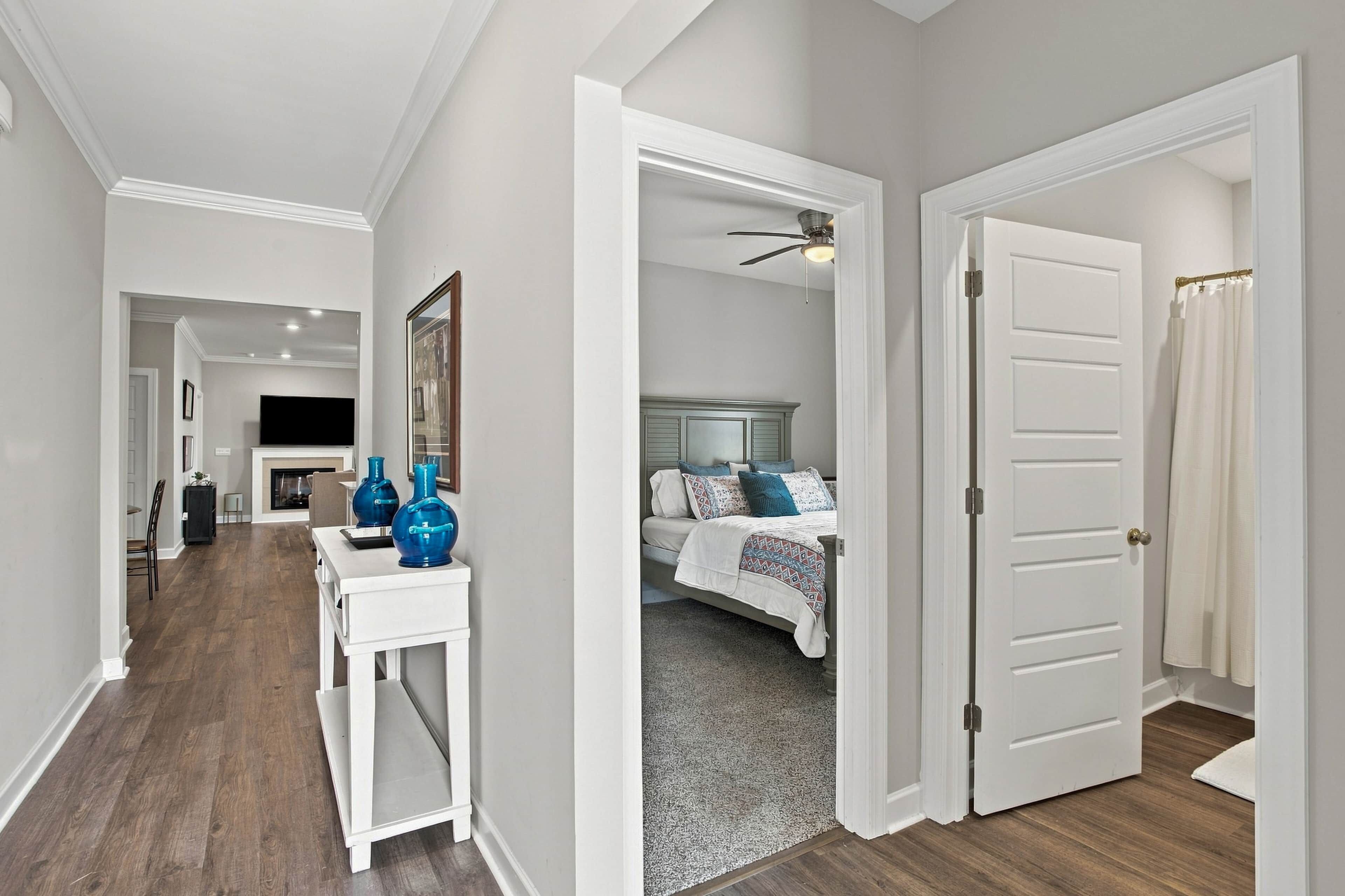 A hallway leading to a bedroom with a bed, a white door, and a ceiling fan.