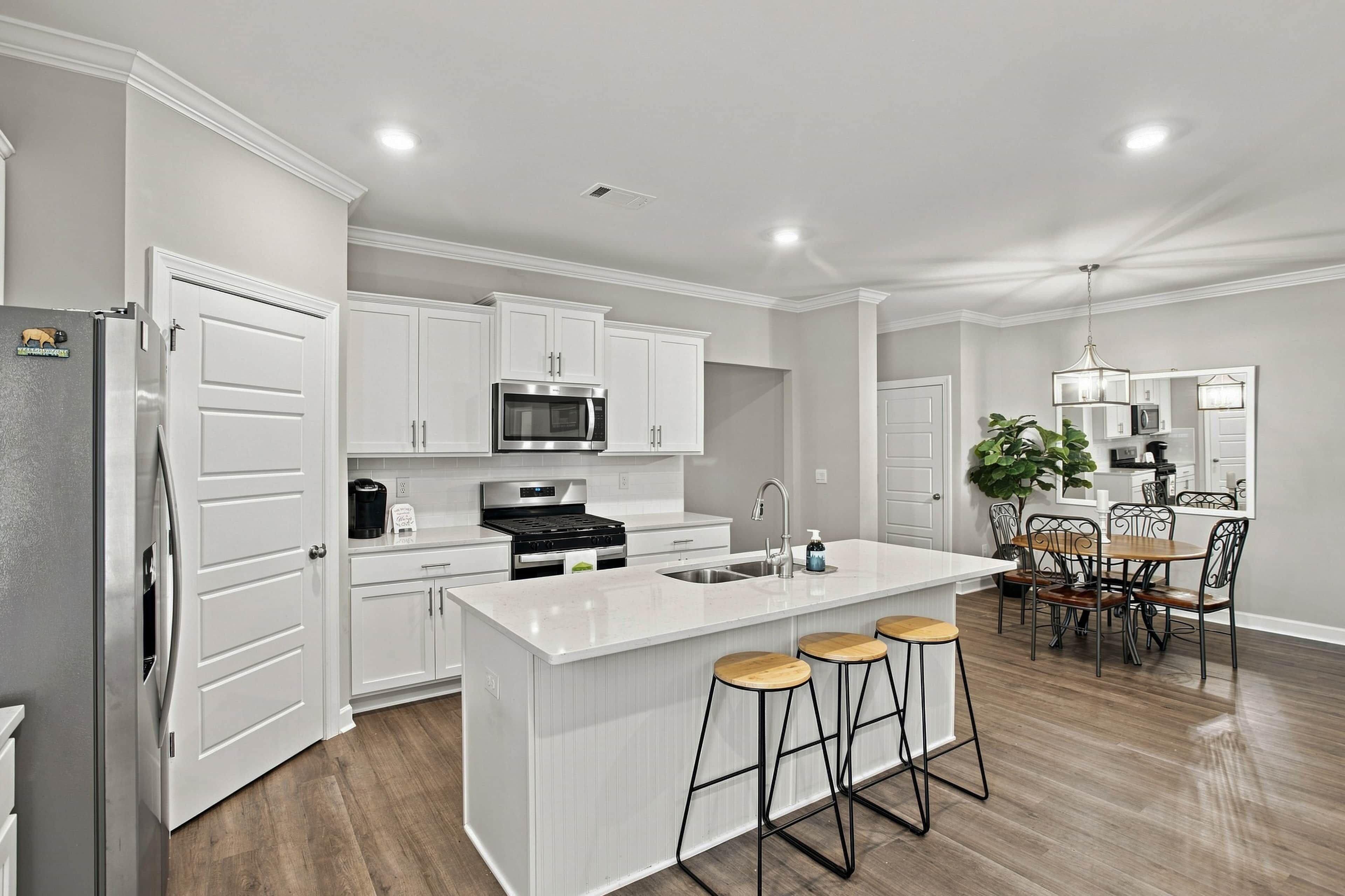 Una cocina moderna con armarios blancos, una isla central con taburetes, un refrigerador de acero inoxidable y un microondas.