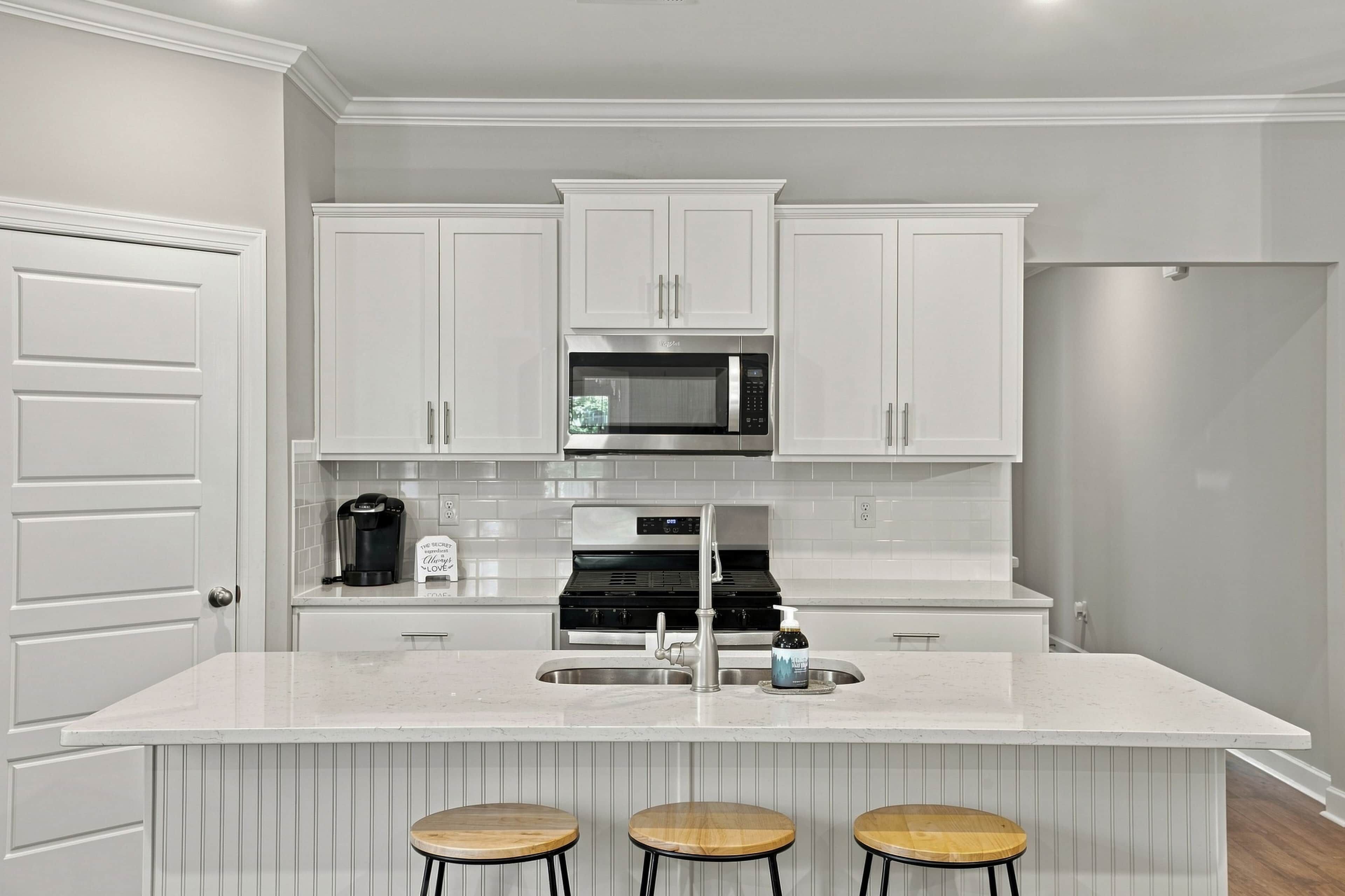 Una cocina moderna con armarios blancos, microondas integrado, estufa y una isla grande con taburetes.