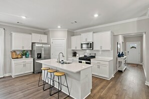 A modern kitchen with white cabinetry, stainless steel appliances, and a central island with stools. - The Loveliest Stay in Auburn (Auburn)