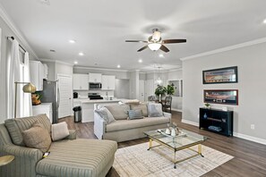 A modern living room with a sofa, coffee table, and a dining area with a chandelier. - The Loveliest Stay in Auburn (Auburn)