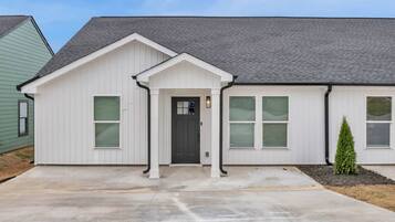 A single-story house with a front porch, a dark front door, and a small tree in the front yard.